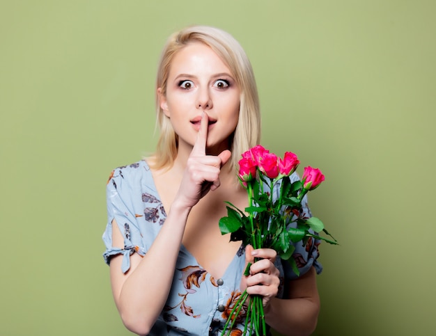 Linda mulher loira de vestido com rosas na parede verde