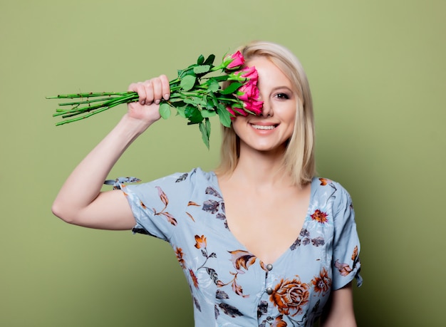 Linda mulher loira de vestido com rosas na parede verde