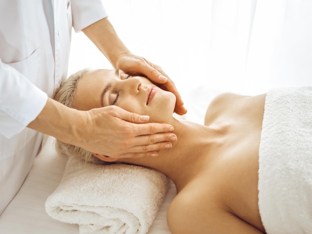 Linda mulher loira desfrutando de massagem facial com os olhos fechados. tratamento relaxante em conceitos de centro de medicina e spa.