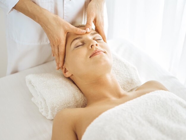 Linda mulher loira desfrutando de massagem facial com os olhos fechados. Tratamento relaxante em conceitos de centro de medicina e spa.
