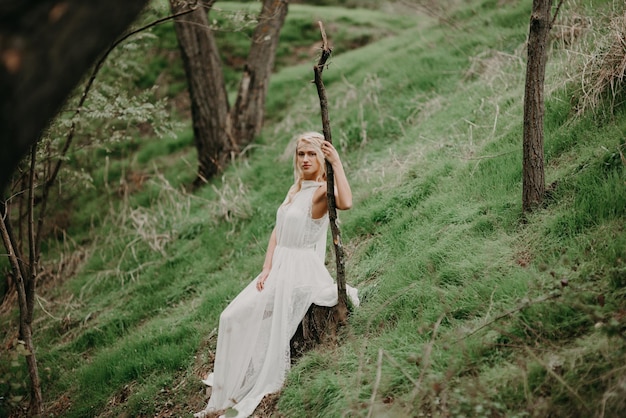 Linda mulher loira em um vestido branco na floresta