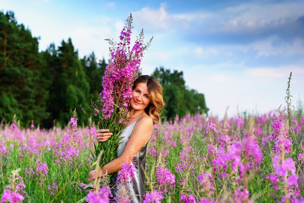 Linda mulher loira em um vestido cinza relaxando com um ramo de flores em um prado de erva.