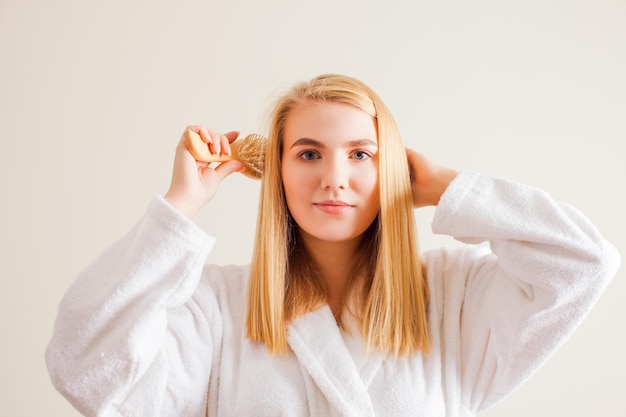 Linda mulher loira escovando o cabelo depois do banheiro Cuidados com o cabelo e conceito de tratamento