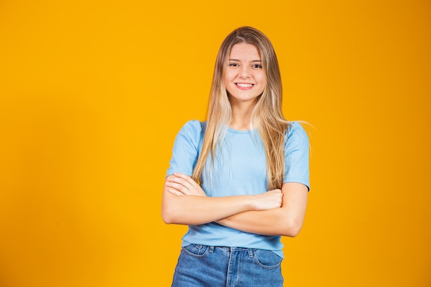 Linda mulher loira isolada em fundo amarelo. linda mulher caucasiana, vestindo camiseta casual rosto feliz, sorrindo com os braços cruzados, olhando para a câmera. pessoa positiva.