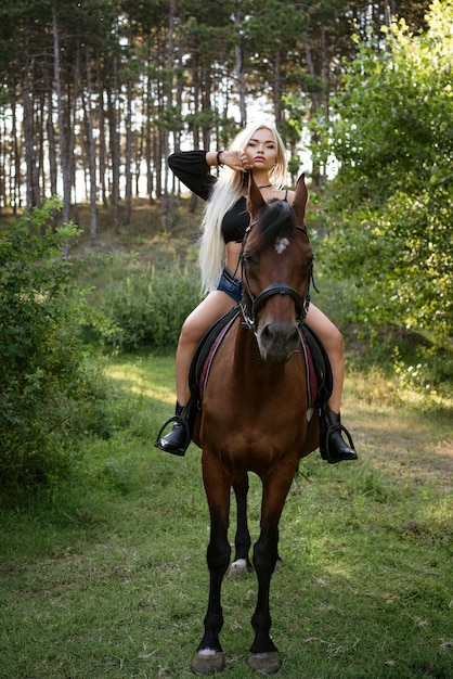 Linda mulher loira parada com um cavalo na natureza na floresta
