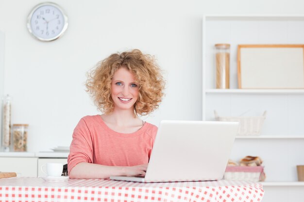 Linda mulher loira relaxando com o laptop enquanto estava sentada na cozinha