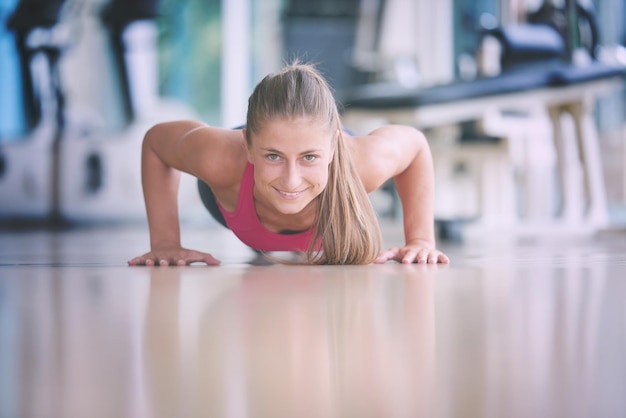 Linda mulher loira se aquecendo e fazendo algumas flexões na academia