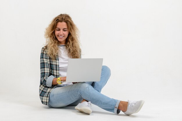 Linda mulher loira sentada no chão com o laptop na parede branca