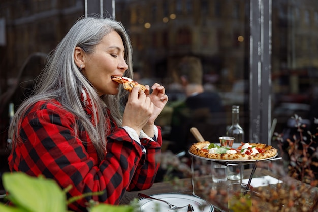 Linda mulher madura asiática comendo pizza no terraço do café