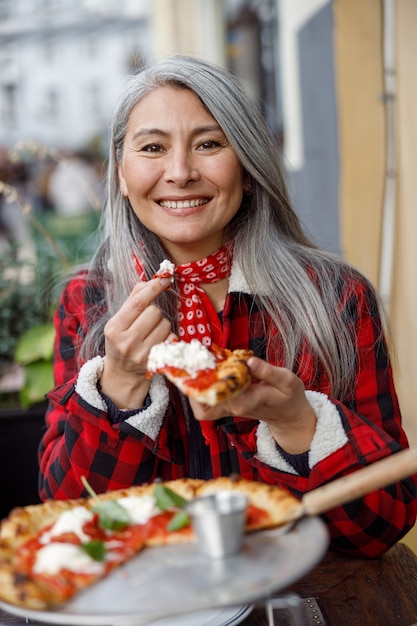 Linda mulher madura asiática comendo pizza no terraço do café