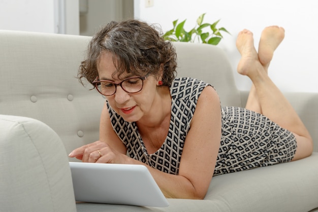 Linda mulher madura com um tablet no sofá