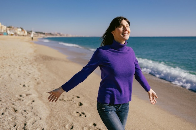 Linda mulher madura relaxando respirando ar fresco em um dia ensolarado de inverno na praia