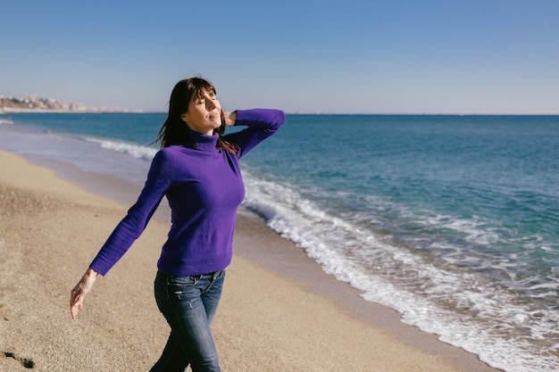 Linda mulher madura relaxando respirando ar fresco em um dia ensolarado de inverno na praia