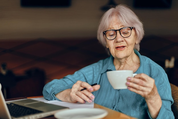 Linda mulher madura sentada em um café com uma xícara de café e um laptop Freelancer trabalha inalterado