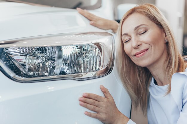 Foto linda mulher madura sorrindo abraçando seu novo automóvel
