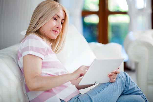 Linda mulher madura usando tablet eletrônico em casa