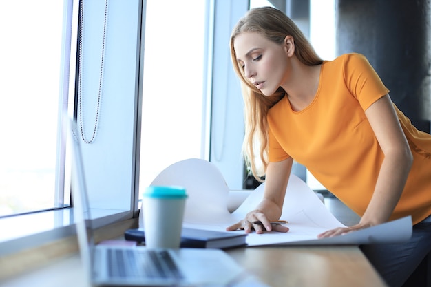 Linda mulher moderna está escrevendo algo na planta enquanto trabalhava no escritório criativo.