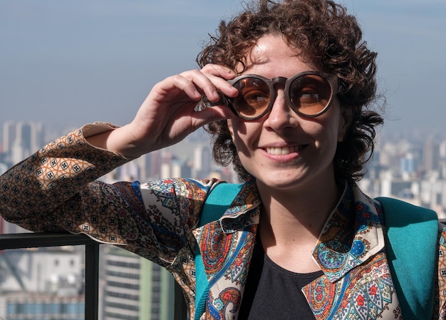 Linda mulher moderna posando para a câmera usando óculos escuros com a cidade de São Paulo em segundo plano