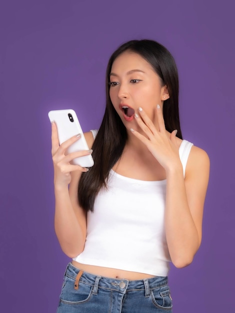 Linda mulher morena asiática linda garota de regata branca jogando um telefone inteligente isolado em fundo roxo celular usa um banco on-line para pagar compras on-line
