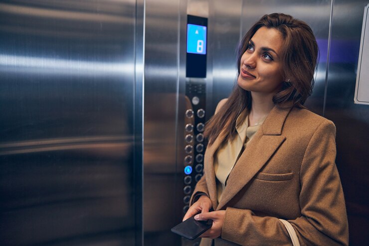 Linda mulher morena com casaco da moda ficar sozinha no elevador com o celular nas mãos e sorrindo