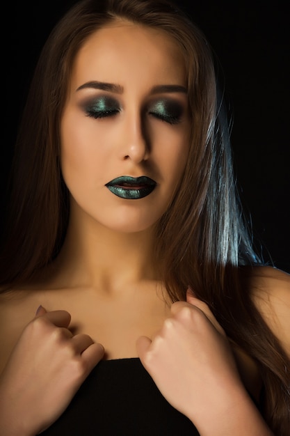 Linda mulher morena com maquiagem criativa verde metálico posando com os olhos fechados. Closeup retrato em estúdio em um fundo escuro