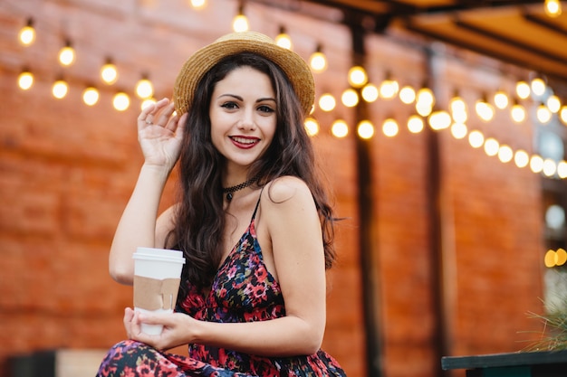 Linda mulher morena com olhos escuros e lábios vermelhos, aproveitando seu tempo livre na cafeteria, bebendo café ou chá quente