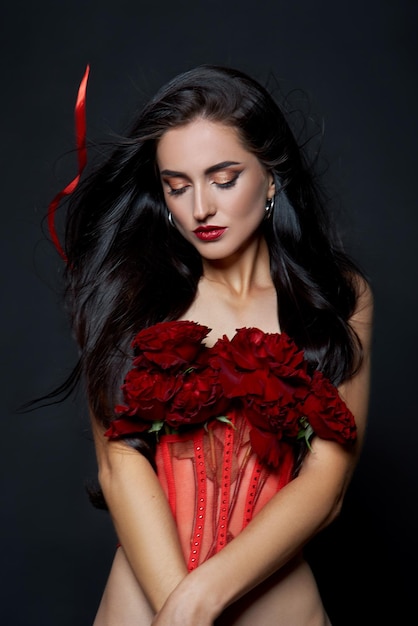 Linda mulher morena com um buquê de flores rosas vermelhas no espartilho vermelho. Cabelo comprido, retrato de arte corporal nude