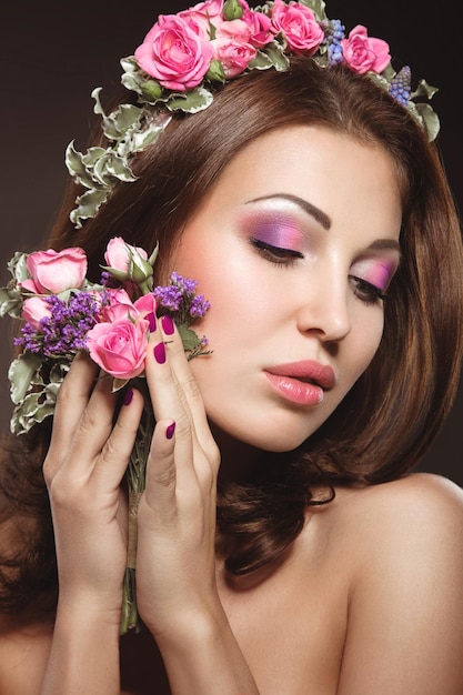 Linda mulher morena com uma maquiagem romântica suave lábios cor de rosa segurando flores A beleza do rosto