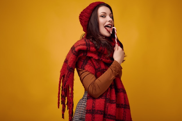 Linda mulher morena de chapéu vermelho com cachecol de malha grande, segurando um doce