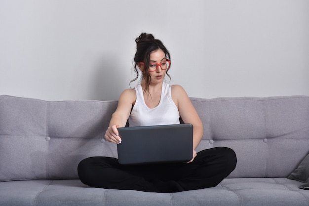Linda mulher morena de óculos vermelhos no sofá usando laptop
