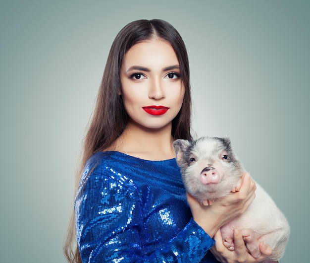 Linda mulher morena de vestido azul brilhante segurando o porquinho