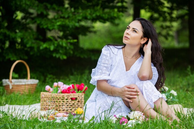 Linda mulher morena descansando no parque, sentada em uma toalha de piquenique, relaxando na natureza