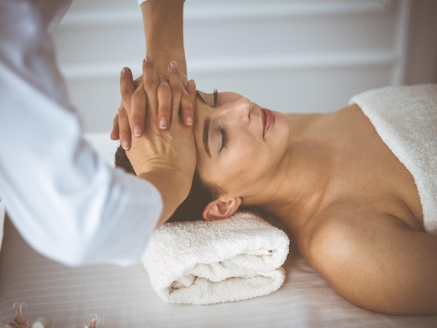 Linda mulher morena desfrutando de massagem facial com os olhos fechados, confortável e feliz. Tratamento relaxante em conceitos de centro de medicina e spa.