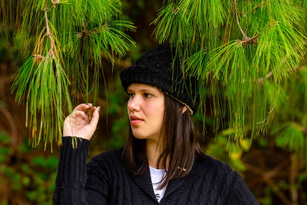 Linda mulher morena em meio a ramos da floresta de pinheiros e folhas em um dia de inverno