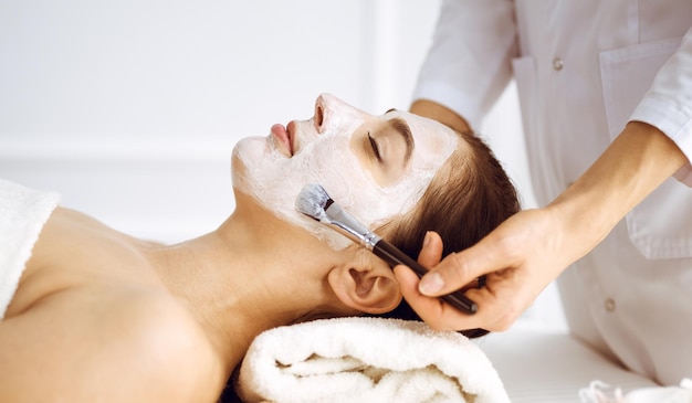 Linda mulher morena gostando de aplicar máscara cosmética com os olhos fechados. Tratamento relaxante em conceitos de centro de medicina e spa.