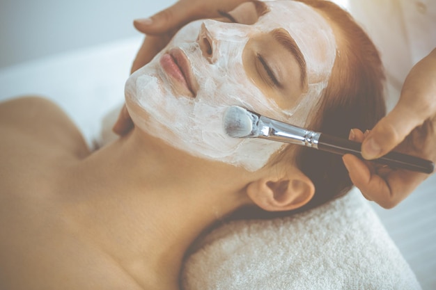 Linda mulher morena gostando de aplicar máscara cosmética com os olhos fechados. Tratamento relaxante em conceitos de medicina e spa.