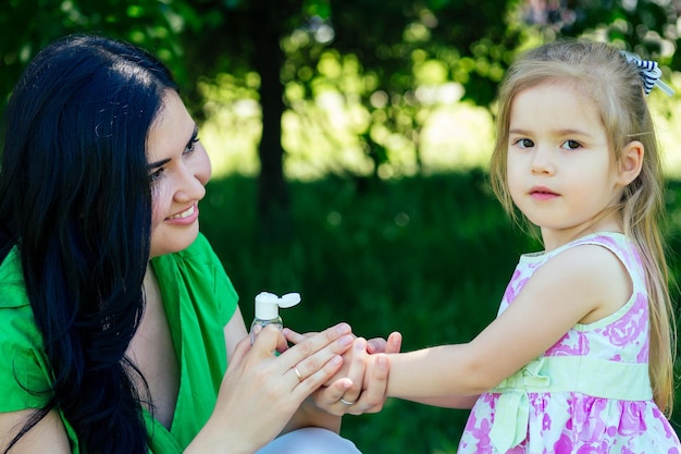 Linda mulher morena mãe solteira aplica gel antibacteriano antisséptico na mão da filha no parque de verão