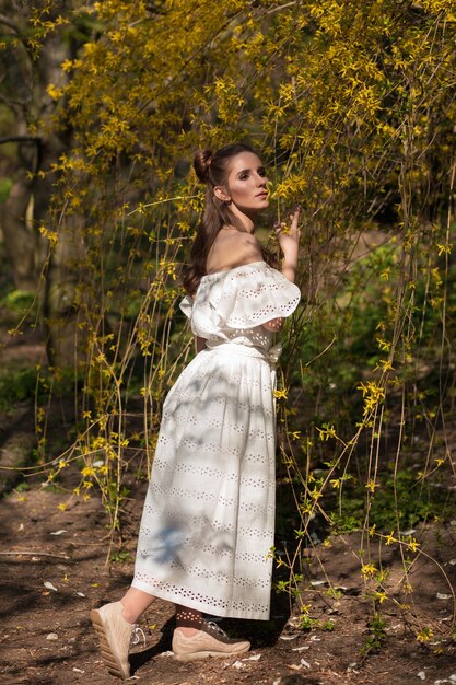 Linda mulher morena posando perto da árvore florescendo em um vestido de renda branca