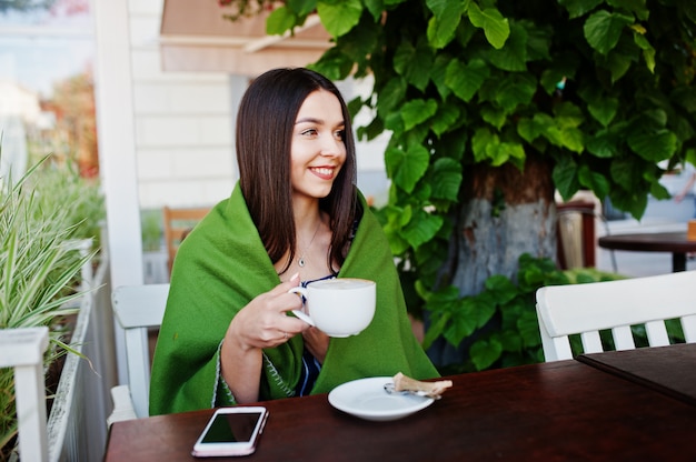 Linda mulher morena, sentada em cima da mesa no café capa xadrez com xícara de café.