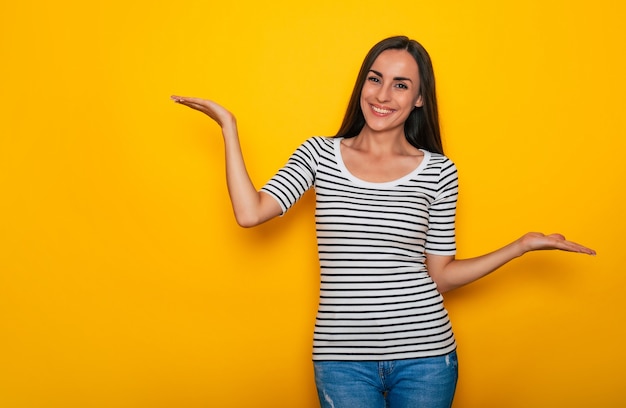 Linda mulher morena sorridente moderna em trajes casuais posando contra uma parede amarela