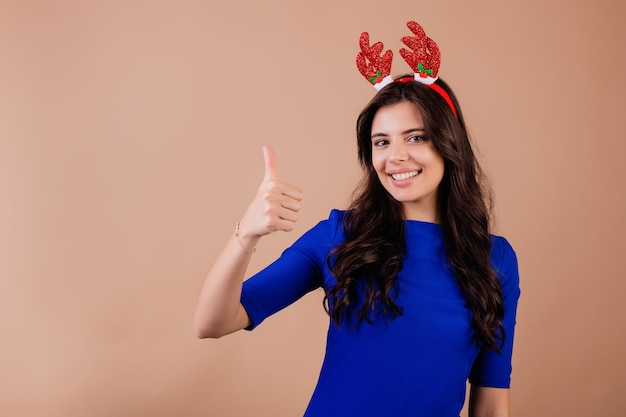 Linda mulher morena sorridente, mostrando os polegares e vestindo chrismas aro isolado sobre marrom