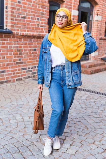 Linda mulher muçulmana árabe usando hijab amarelo, elegante retrato feminino ao longo da rua da cidade.