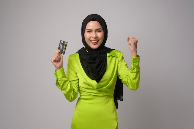 Linda mulher muçulmana com hijab segurando o cartão de crédito sobre o estúdio de fundo branco