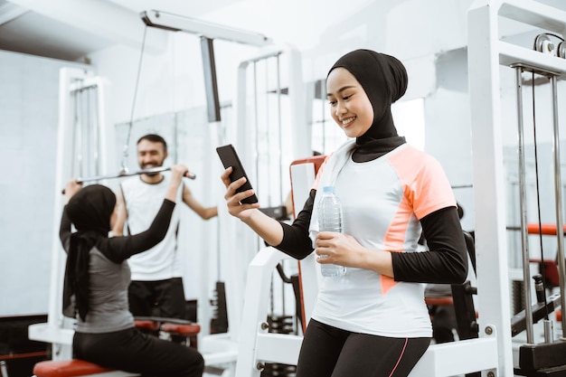 Linda mulher muçulmana desportiva fazendo uma pausa depois de se exercitar na academia sentada no chão e nós