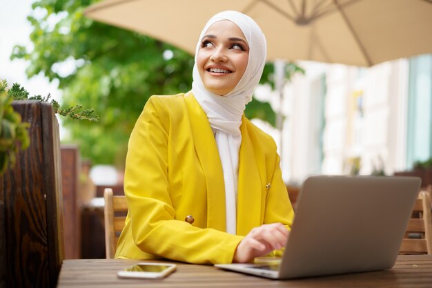 Linda mulher muçulmana sorridente com laptop no café