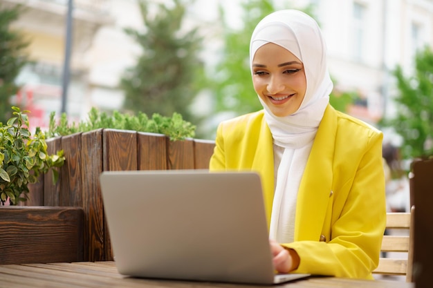 Linda mulher muçulmana sorridente com laptop no café