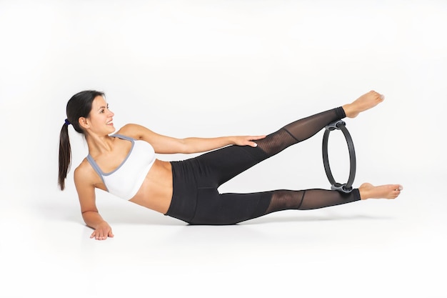 Linda mulher musculosa fazendo exercício com aro de mola em um fundo branco Pilates Ring