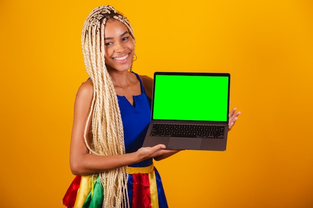 Linda mulher negra brasileira com tranças vestindo roupas para carnaval Segurando notebook mostrando tela verde de croma