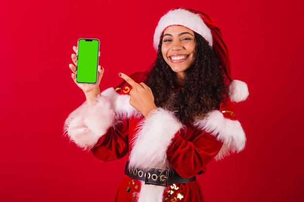 Linda mulher negra brasileira vestida de papai noel roupas de natal segurando celular com tela cromática