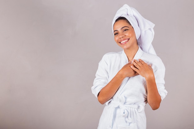 Linda mulher negra brasileira vestindo roupão e toalha com as mãos no coração gratidão spa estética delicadeza bem estar